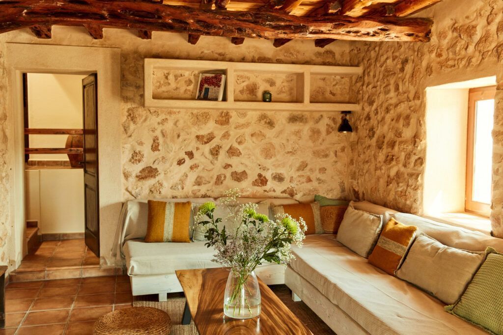 Rincón con sofá familiar en casa con vigas de madera y pared de piedra en Sa Païssa den Botja Ibiza